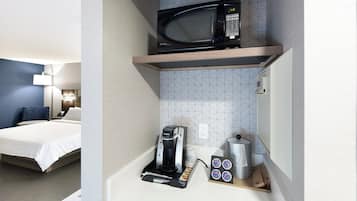 A hotel room with a bed, a microwave, a coffee machine, and a tray with coffee cups and a coffee pod.