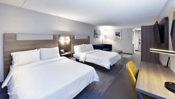 Une chambre d’hôtel avec deux lits, un bureau, une chaise, une télévision et des œuvres d’art accrochées aux murs.