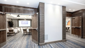 A conference room with a large screen displaying a presentation, a wooden panel wall, and a carpeted floor.