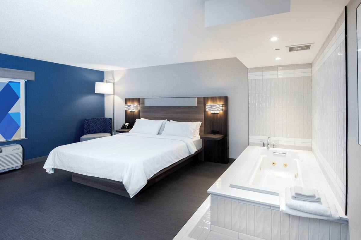 A modern hotel room with a large bed, a separate bathroom with a bathtub, and a desk with a lamp.