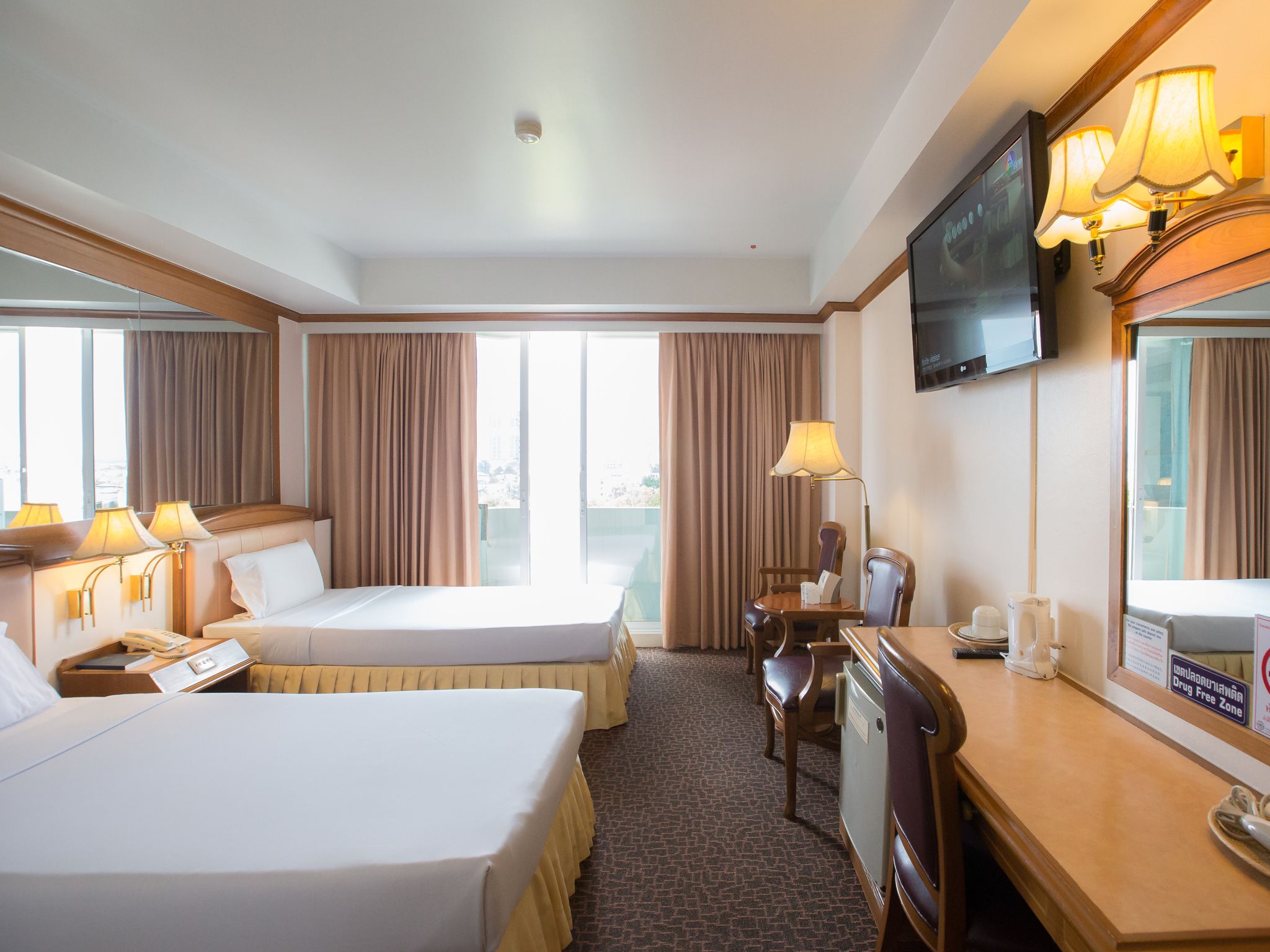 Habitación de hotel con dos camas, un escritorio, una silla, un televisor y una ventana con cortinas.