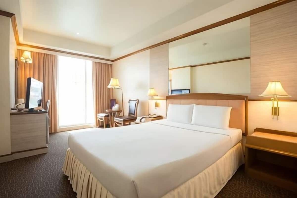 Una habitación de hotel con una cama grande, un escritorio con una silla, un televisor y una lámpara de escritorio.