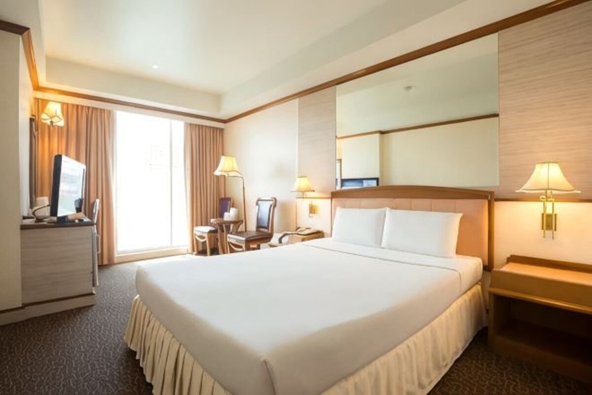 A hotel room with a large bed, a desk with a chair, a television, and a desk lamp.