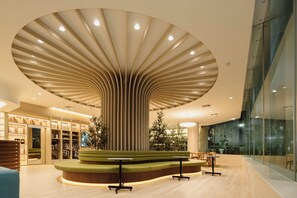 Un intérieur moderne avec un espace salon central, un plafond aux lignes courbes et un mur de verre d’un côté.