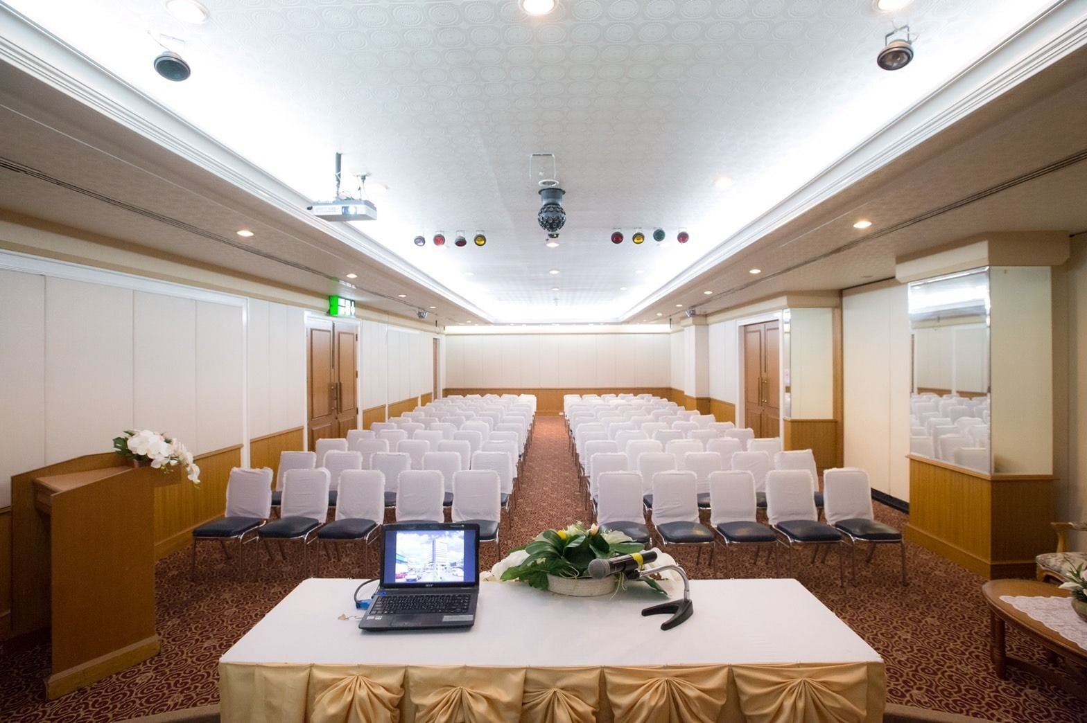 A conference room with rows of white chairs, a laptop on a table, and a microphone.