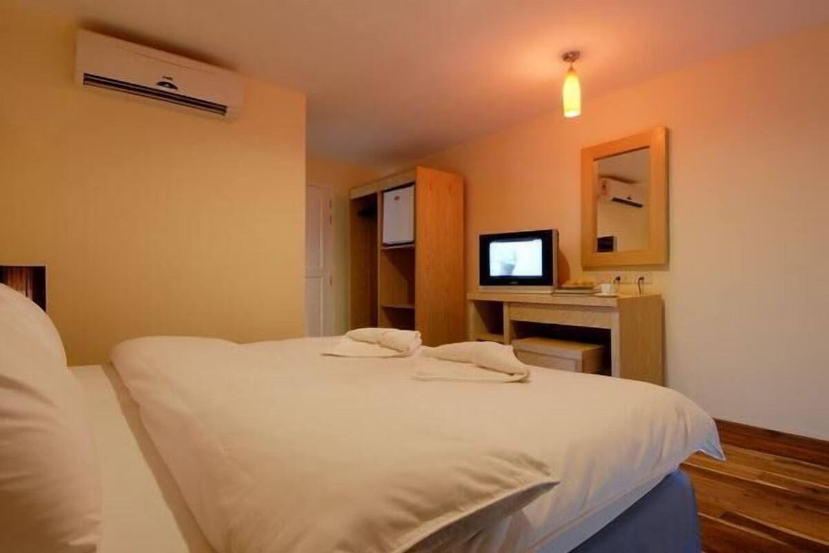 Hotellihuone, jossa on kaksi sänkyä, televisio, peili ja puinen vaatekaappi.