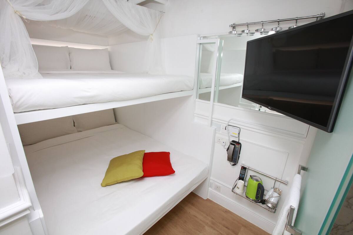 Een slaapkamer met stapelbed, televisie, nachtkastje met waterkoker en een stopcontact.