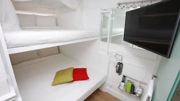 A bunk bed room with a television, a bedside table with a kettle, and a power outlet.