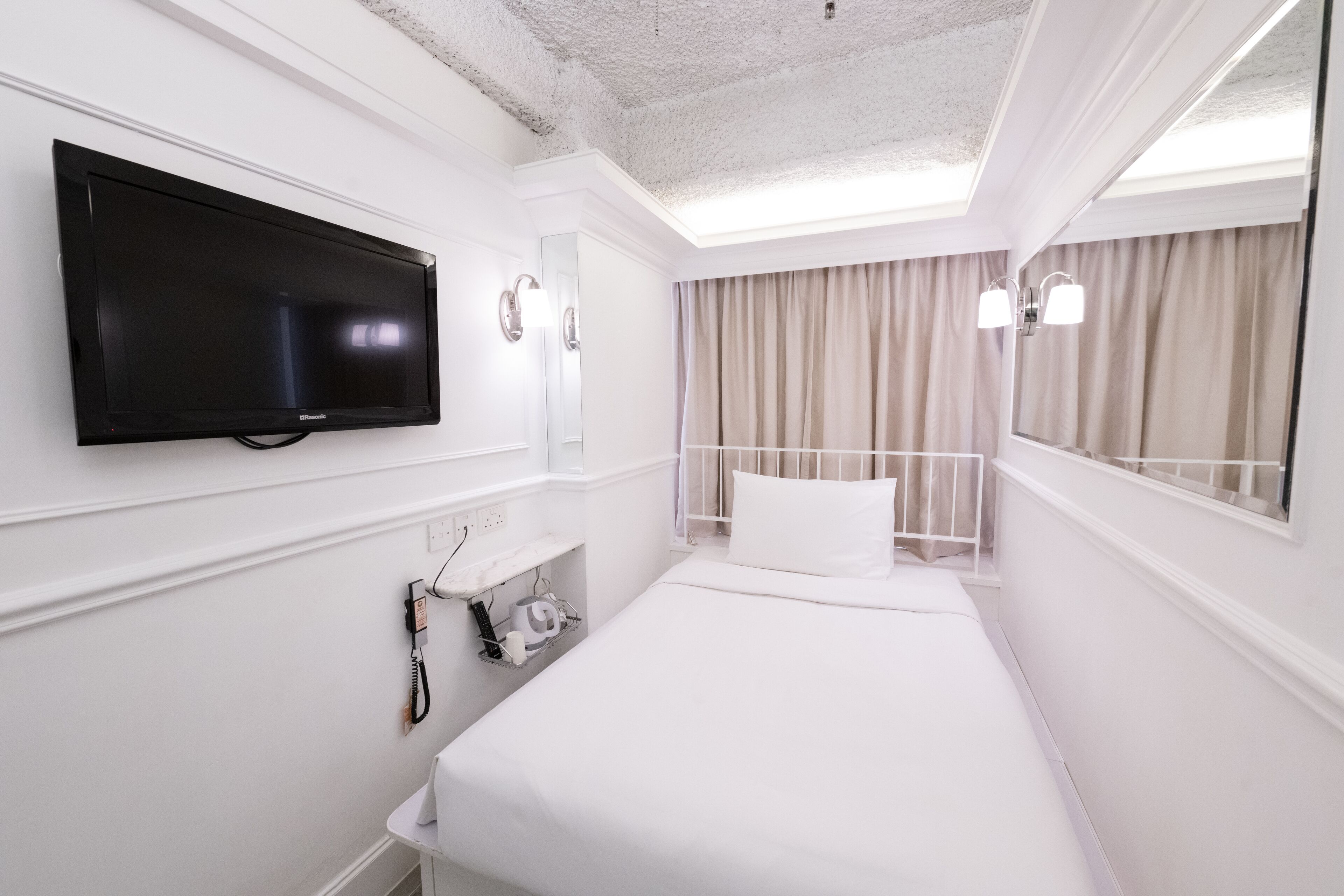 Ein Hotelzimmer mit Bett, Wandfernseher, Nachttisch, Spiegel und einem Vorhangfenster.