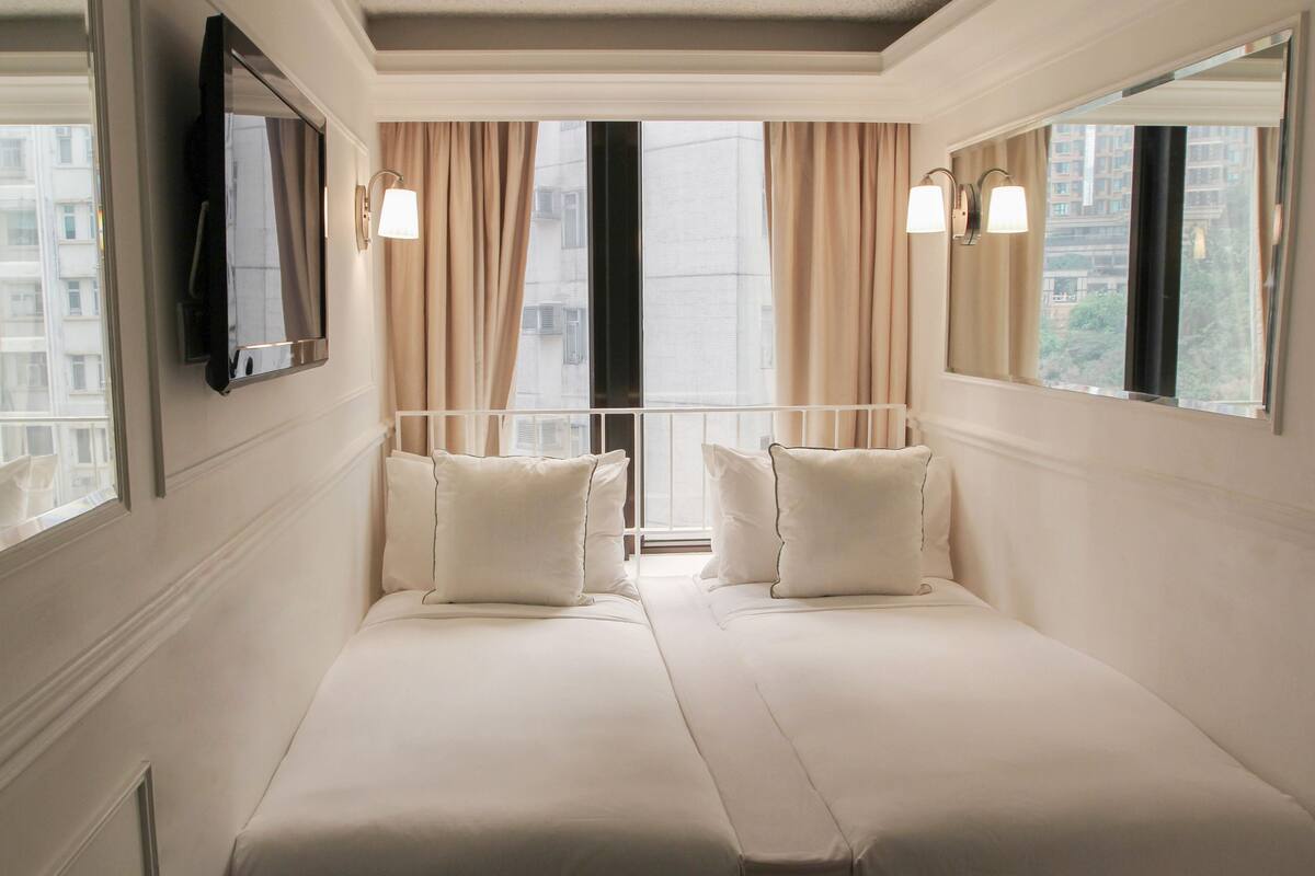 Een hotelkamer met twee bedden, een televisie, een raam met gordijnen en een balkon.