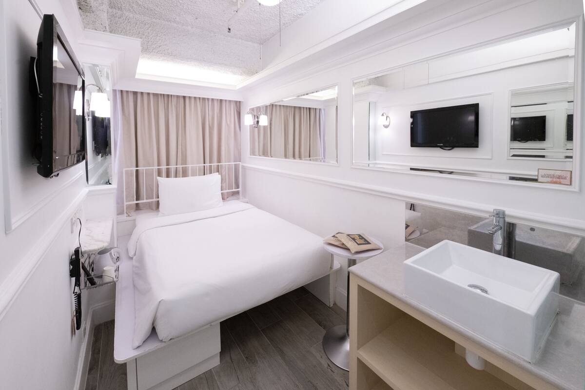 Een hotelkamer met een bed, televisie, wastafel en spiegel.