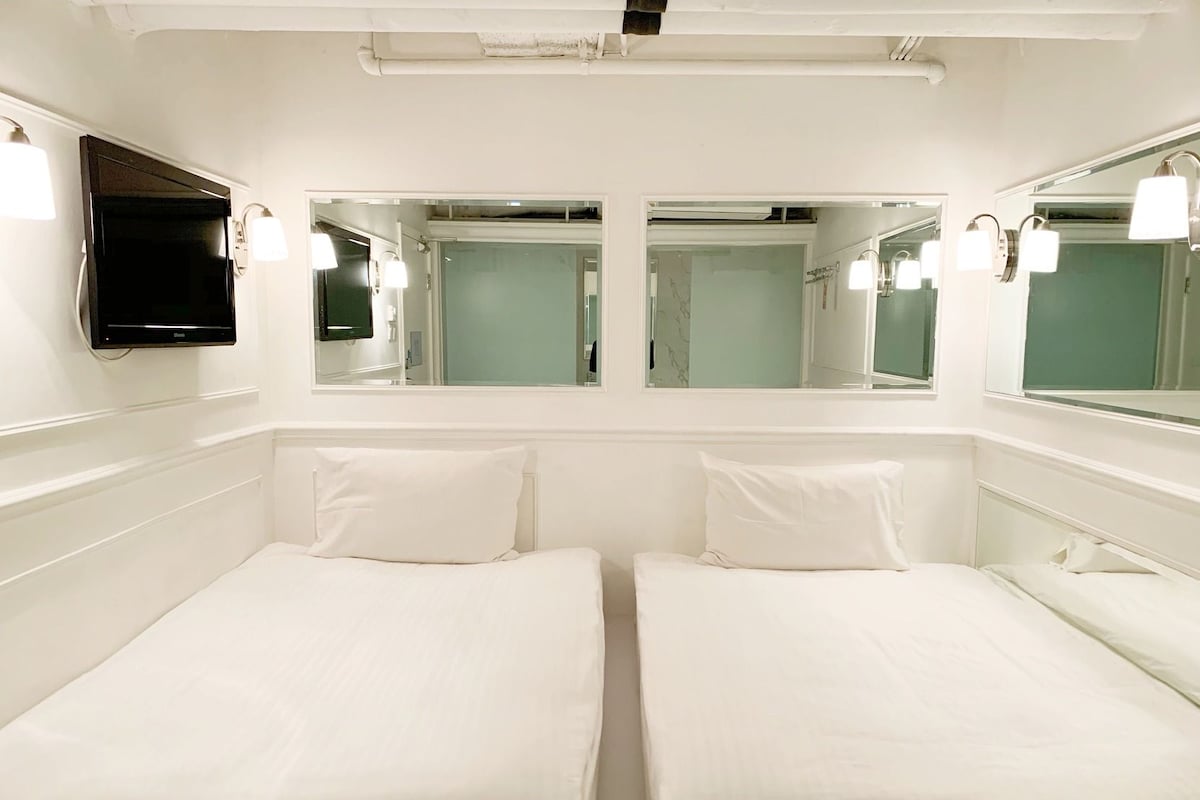 Ein Hotelzimmer mit zwei Einzelbetten, einem an der Wand montierten Fernseher und einem großen Spiegel über den Betten.