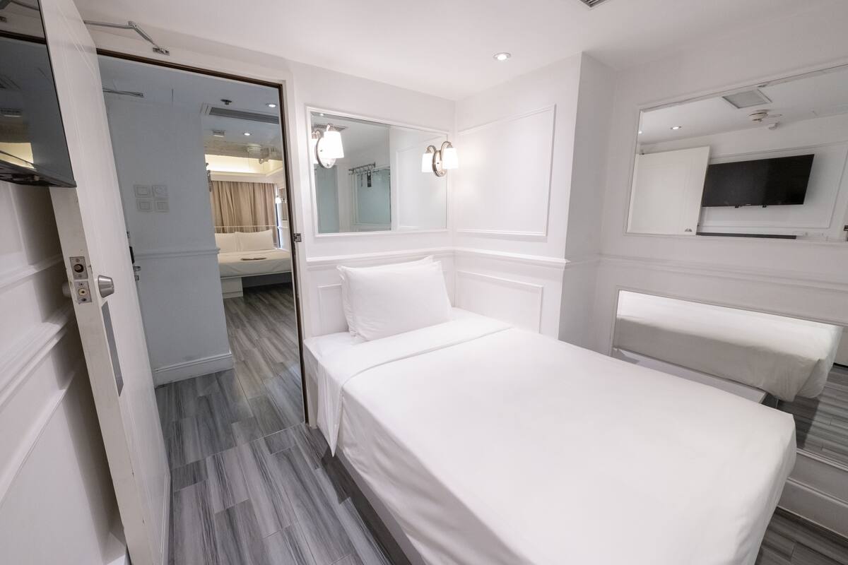 Een hotelkamer met een bed, een spiegel, een televisie en een deur naar een andere kamer.