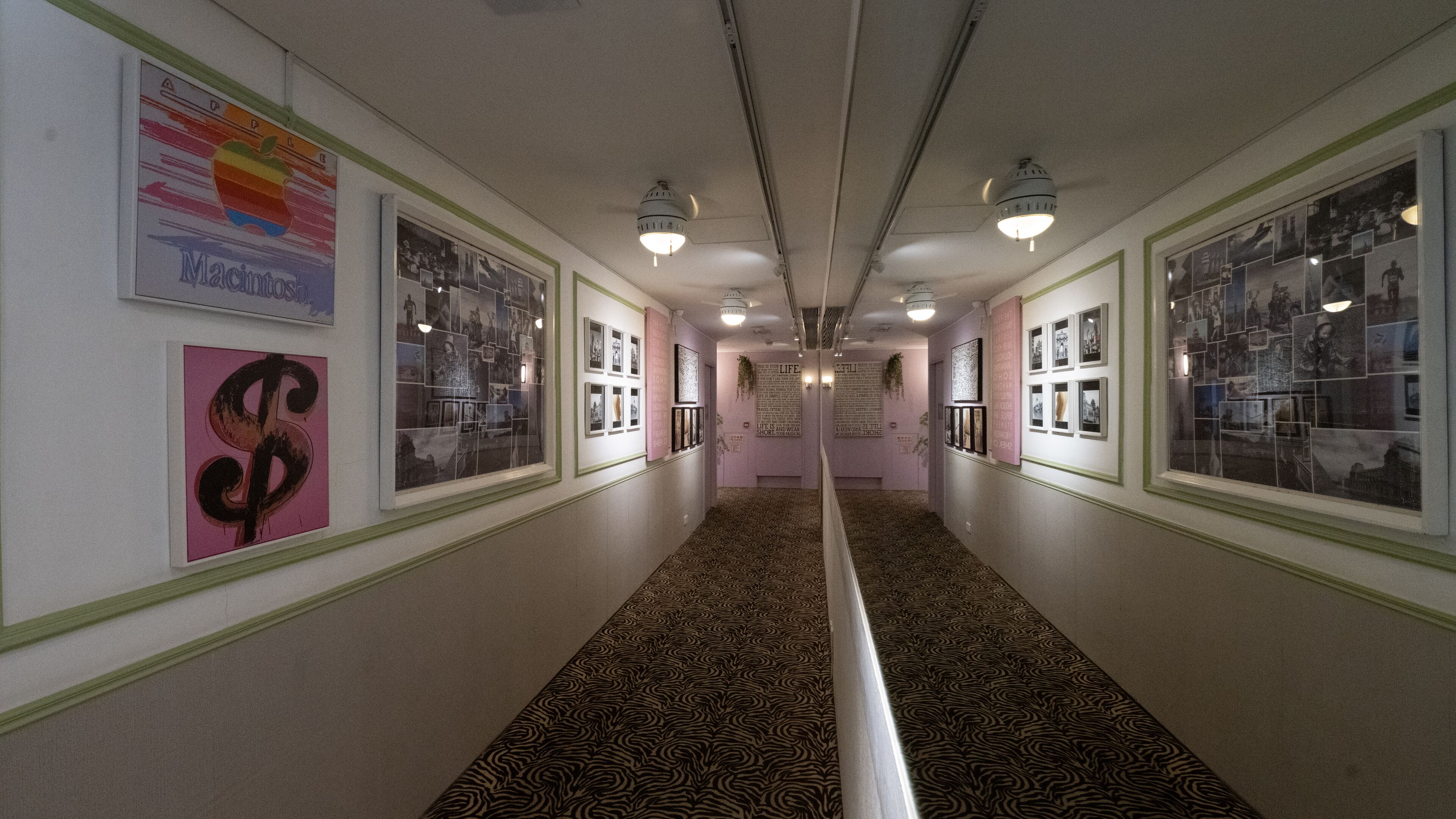 A hallway with framed pictures on the walls, a patterned carpet, and ceiling lights.