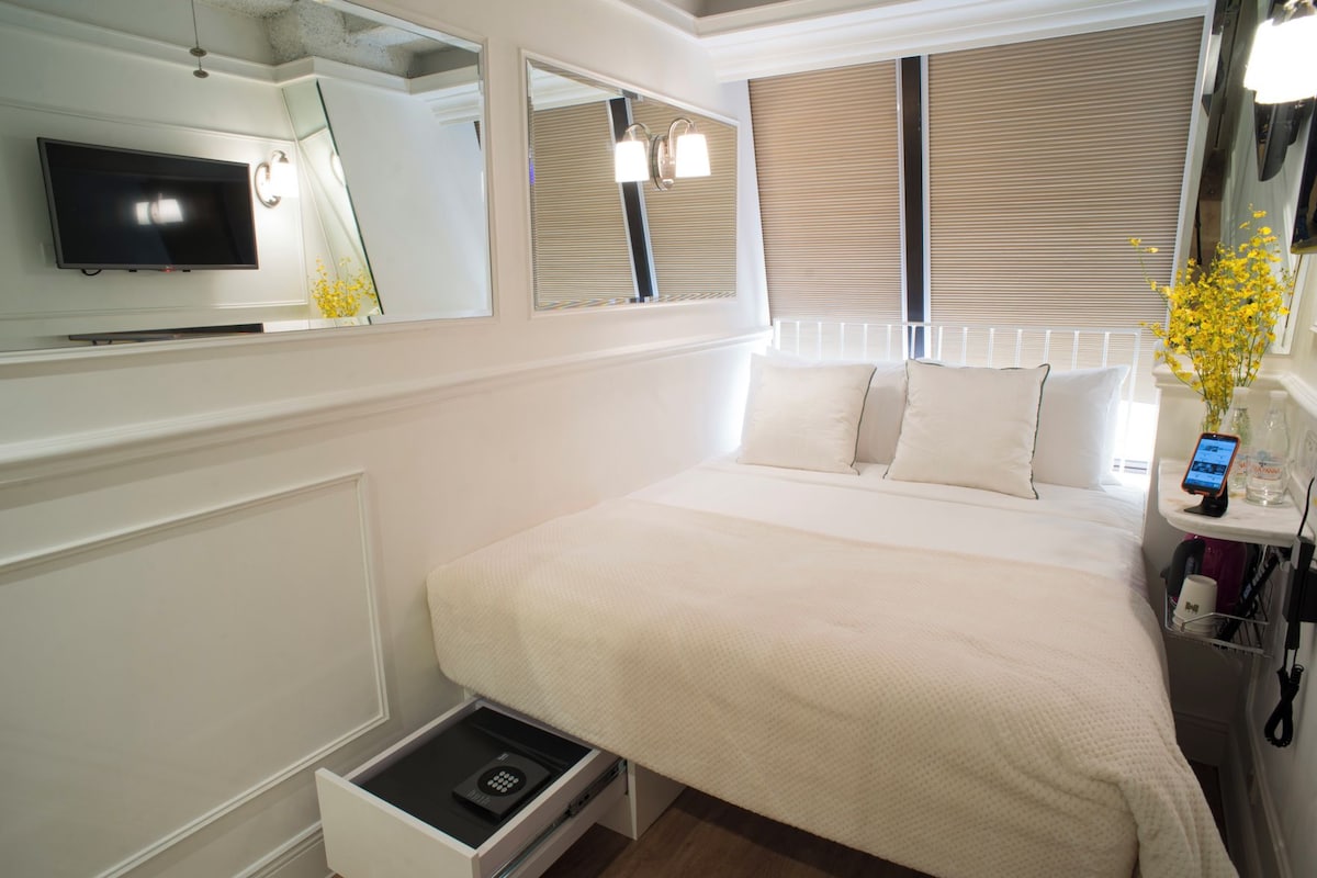 Ein Hotelzimmer mit einem Bett, einem Fernseher, einem Nachttisch mit Telefon und einem Spiegel.