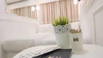 A hotel room with a neatly arranged bed, a white table with a plant and a cup, and a window with curtains.