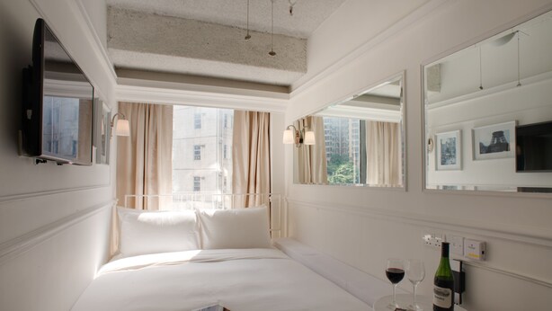 Een hotelkamer met een bed, een nachtkastje met een fles wijn en glazen, een tablet en een aan de muur bevestigde televisie.
