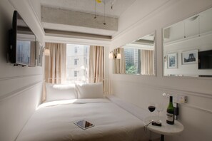 Een hotelkamer met een bed, een nachtkastje met een fles wijn en glazen, een tablet en een aan de muur bevestigde televisie.