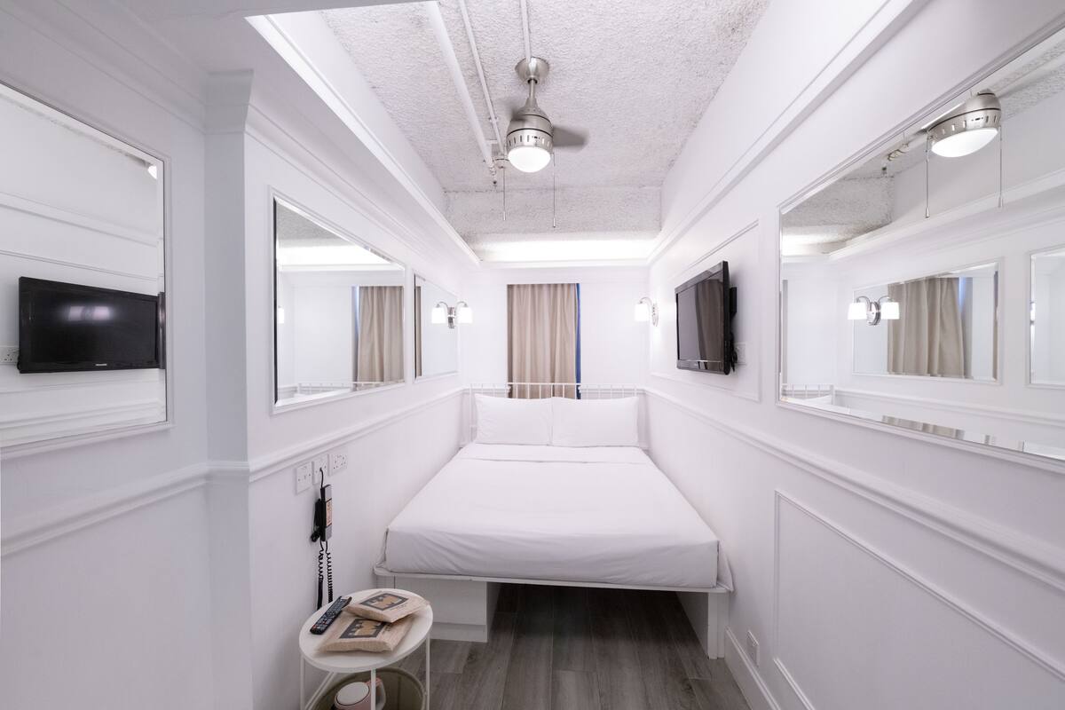 Een hotelkamer met een bed, een televisie, een plafondventilator en een klein tafeltje met een telefoon en boeken.