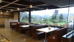 Ein Restaurant mit Sitzboxen, einer Bar und Blick auf einen Garten durch große Fenster.