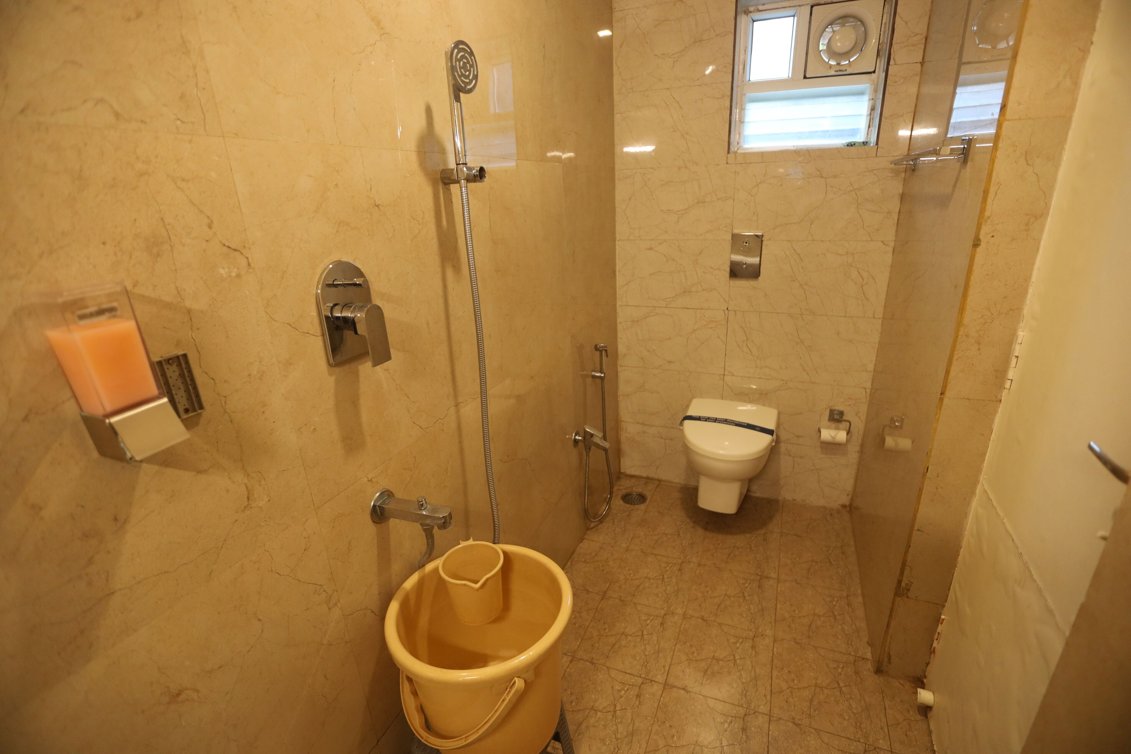 Une petite salle de bain avec une douche, des toilettes et un seau jaune.
