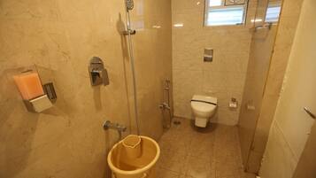 Une petite salle de bain avec une douche, des toilettes et un seau jaune.