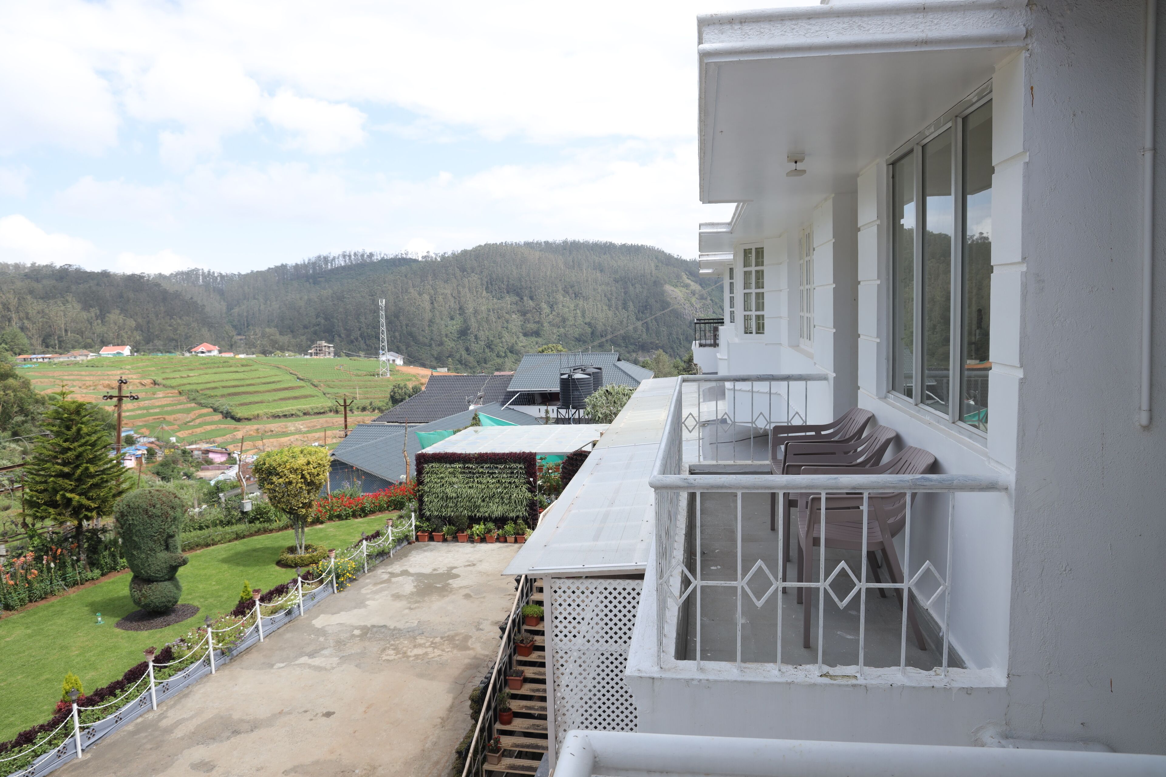 A balcony with a view of a green landscape, a white building, and a clear sky.