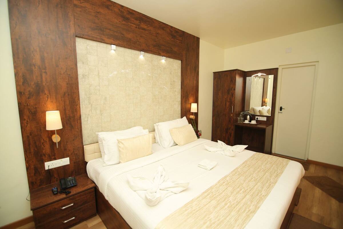 A hotel room with a large bed, wooden headboard, bedside lamps, a dresser, a mirror, and a door.