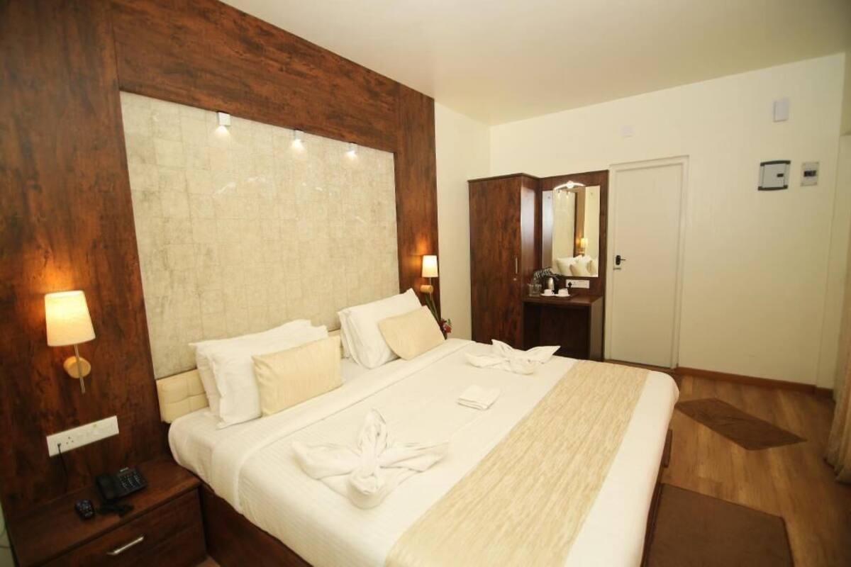 A hotel room with a large bed, wooden headboard, bedside lamps, a mirror, and a door.