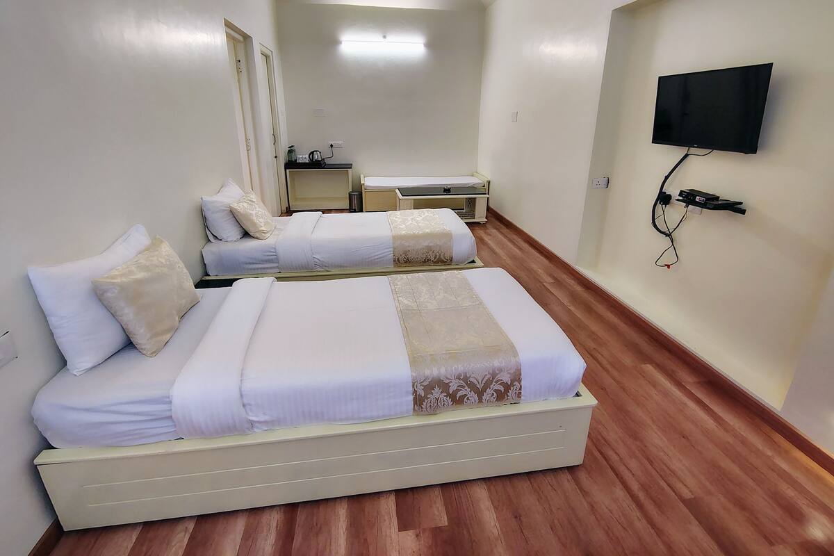A hotel room with two beds, a television mounted on the wall, and a small table with a kettle.