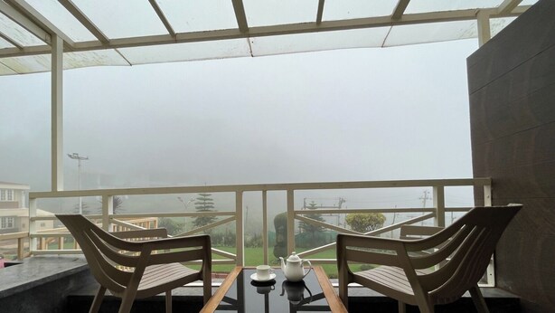 Ein Balkon mit zwei Holzstühlen, einem Glastisch und einem Teekessel.
