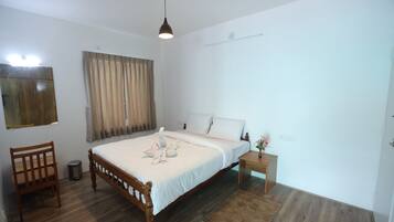 A bedroom with a wooden bed, a bedside table, a chair, a small trash bin, and a window with curtains.