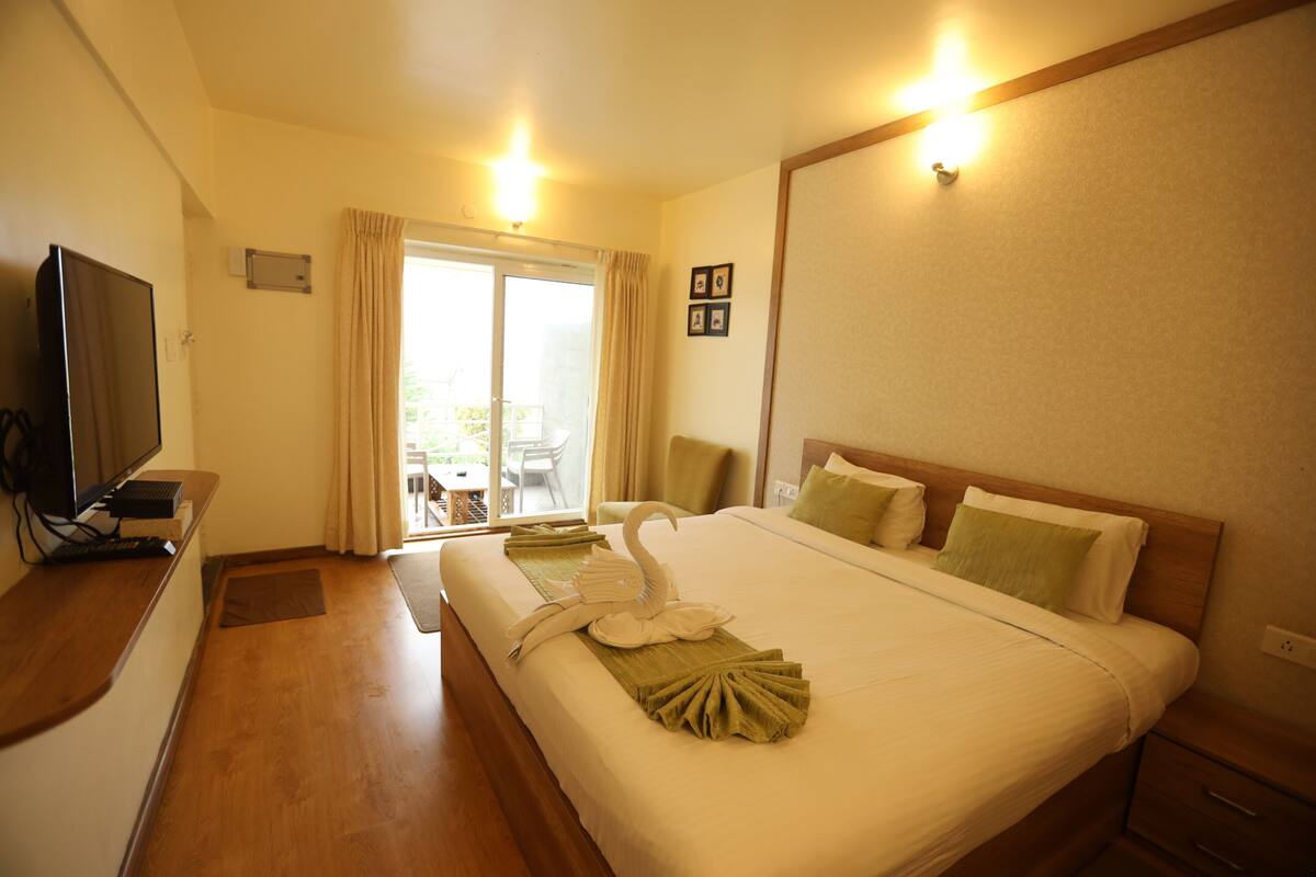 A hotel room with a bed, a television, a desk, and a view of the outdoors through a sliding door.