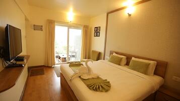 Habitación de hotel con cama, televisión, escritorio y vista al exterior a través de una puerta corrediza.