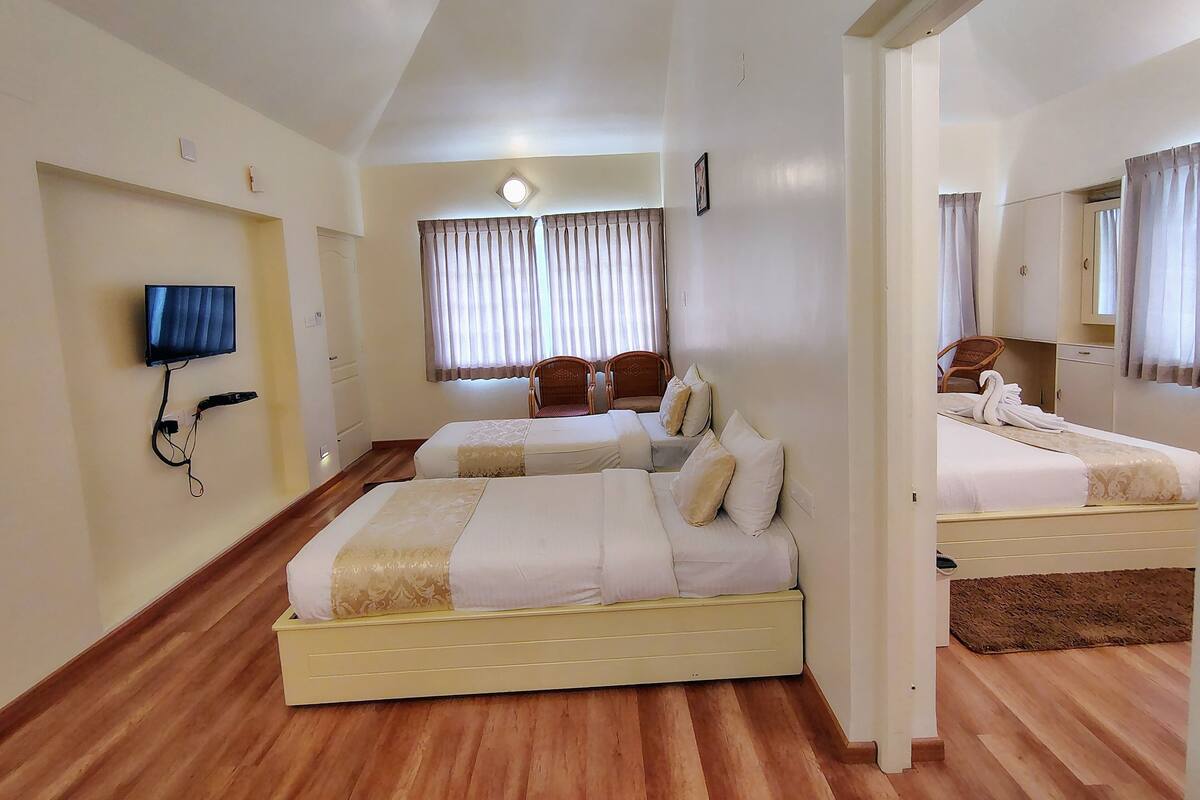 A hotel room with two beds, a TV mounted on the wall, a window with curtains, and a mirror on the wall.