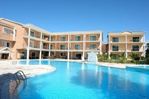 A hotel with a large swimming pool, multiple balconies, and a clear blue sky. - Sunny Golf Hotel (Toamasina)