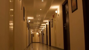 Un largo pasillo bien iluminado con puertas a ambos lados, iluminación empotrada y cuadros en las paredes.