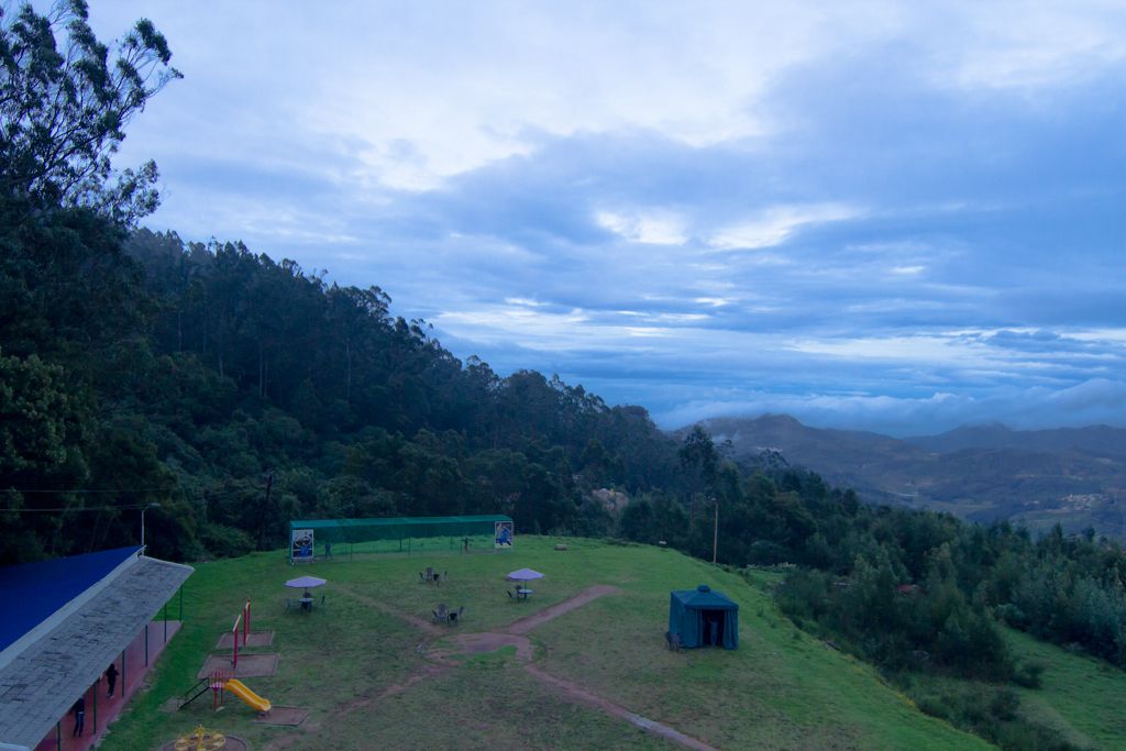 Un área con césped, un parque infantil, una construcción pequeña y un sendero que lleva a una colina.