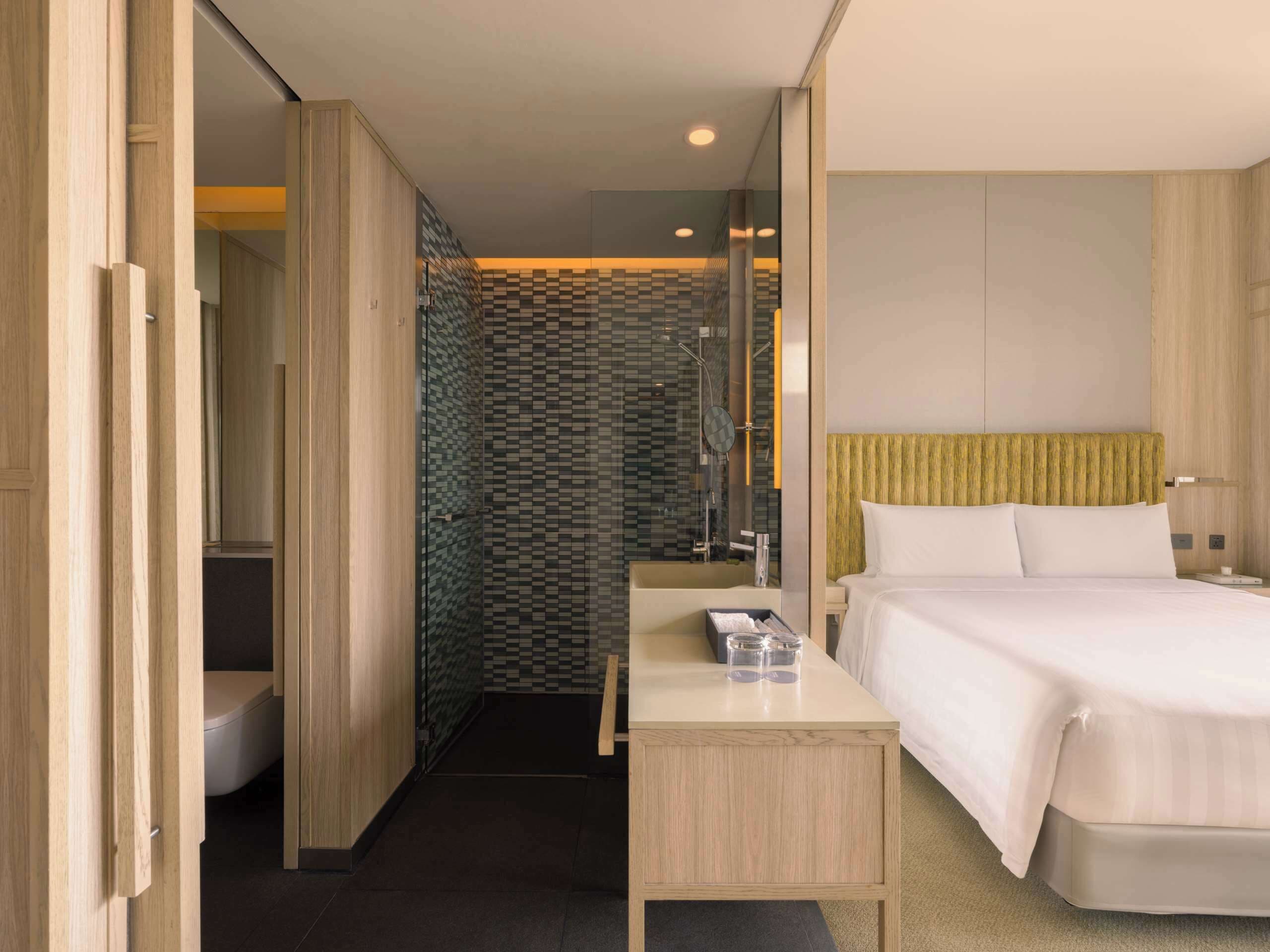 A hotel room with a bed, bedside table, and a shower area.