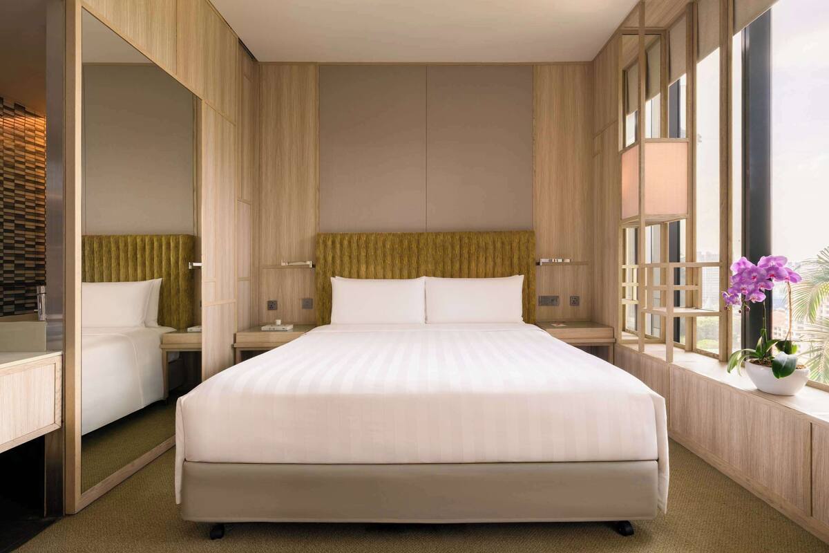Une chambre d’hôtel moderne avec un grand lit, des panneaux de bois, une table de chevet, un miroir et une fenêtre donnant sur un beau paysage.