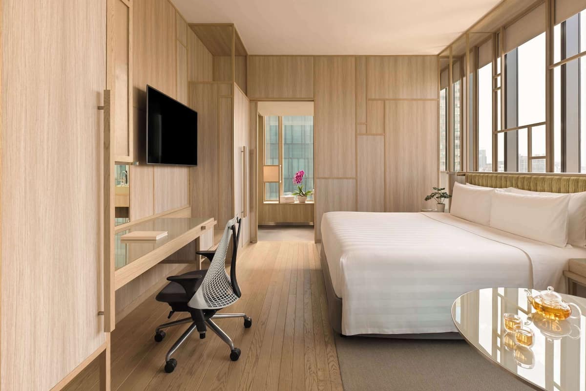 Une chambre d’hôtel moderne équipée d’un lit, d’un bureau avec une chaise, d’une télévision et d’une fenêtre donnant sur la ville.