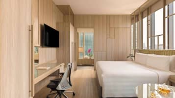 Ein modernes Hotelzimmer mit Bett, Schreibtisch mit Stuhl, Fernseher und Fenster mit Stadtblick.
