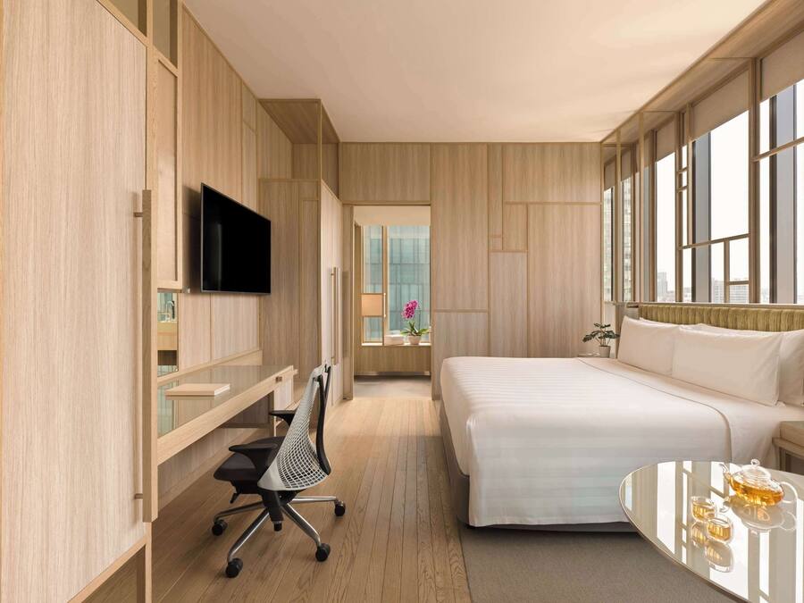 Ein modernes Hotelzimmer mit Bett, Schreibtisch mit Stuhl, Fernseher und Fenster mit Stadtblick.