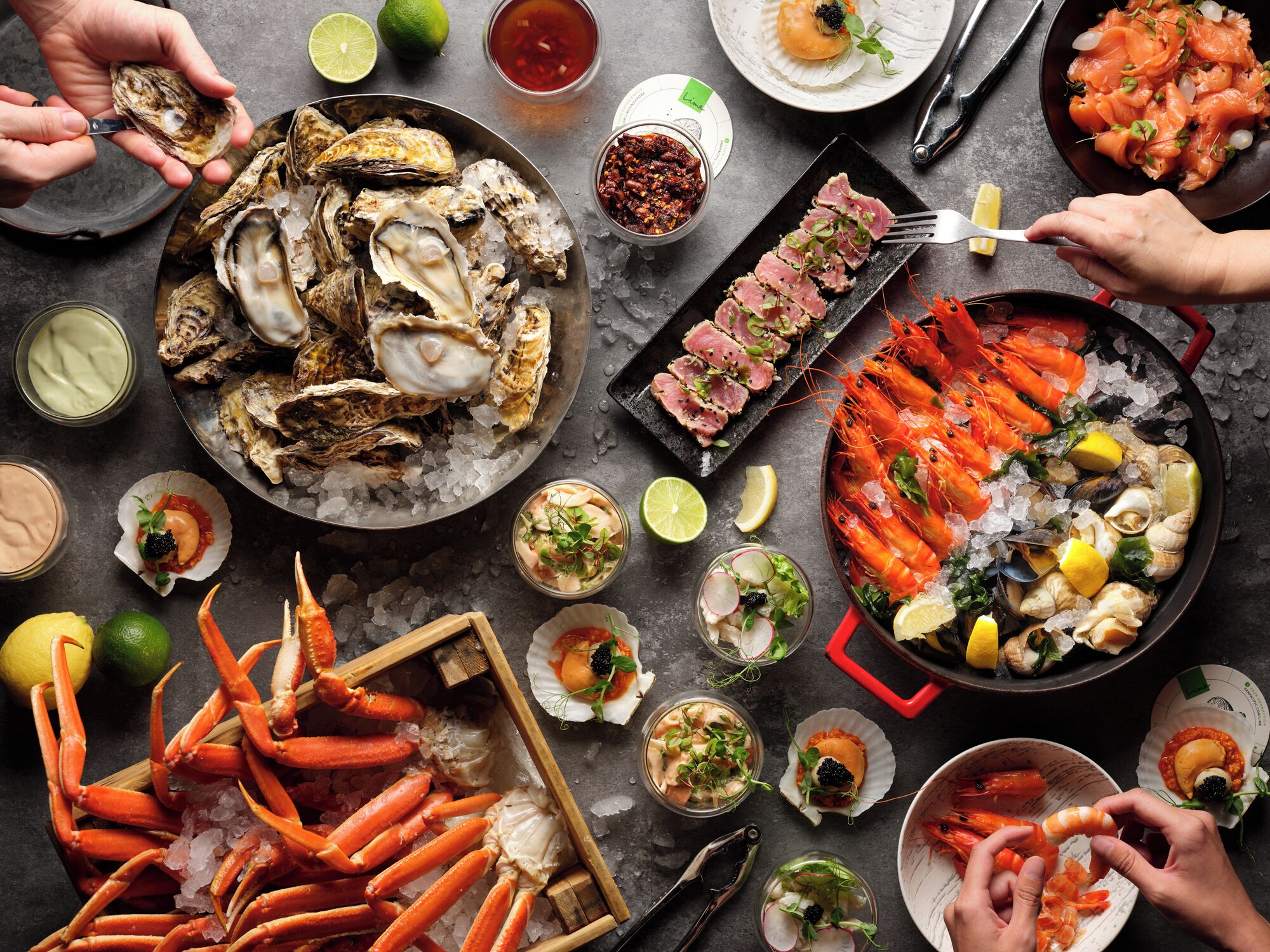 A variety of seafood including oysters, shrimp, and crab legs, served on ice with garnishes and condiments.