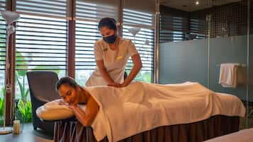 A massage therapy room with a massage table, a massage therapist, and a large window with blinds.