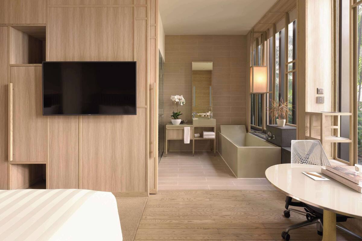 Une chambre d’hôtel moderne dotée d’un grand lit, d’un téléviseur à écran plat fixé au mur, d’une salle de bain avec baignoire et d’un coin repas avec une table ronde.