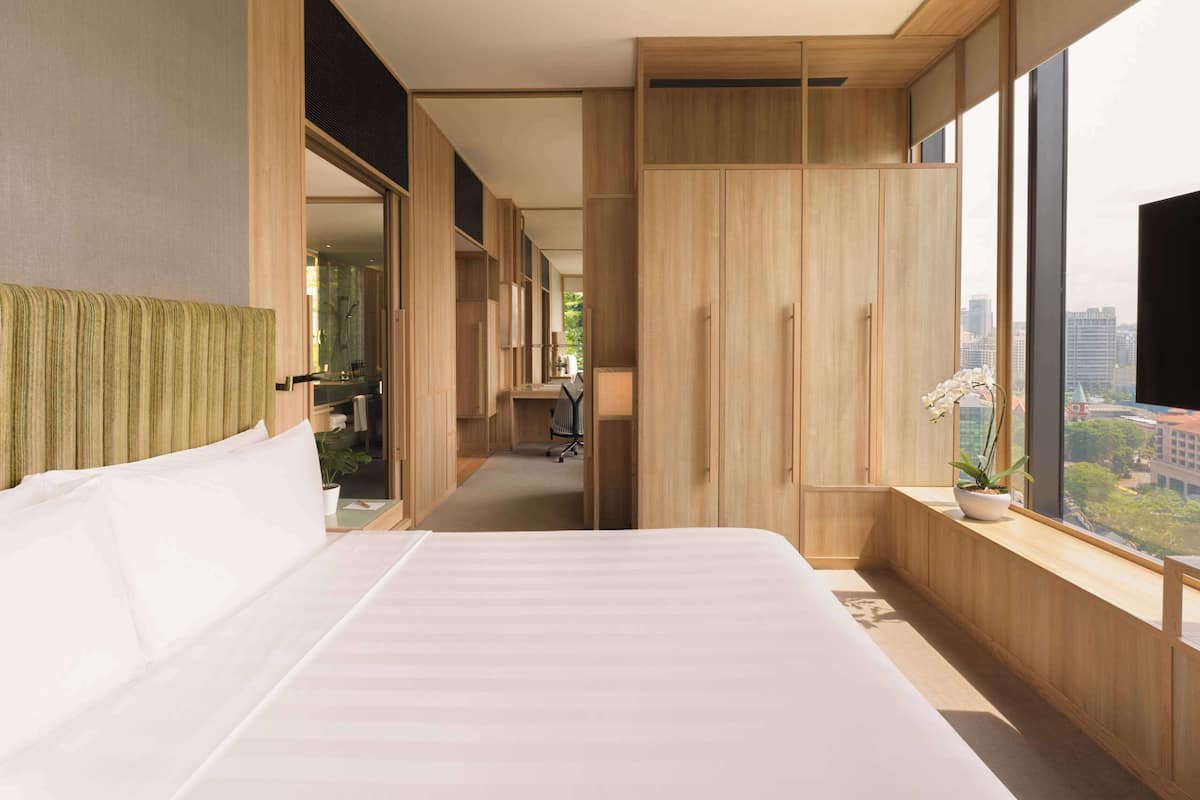 Une chambre moderne avec un grand lit, une armoire en bois et une vue sur la ville grâce à de grandes fenêtres.