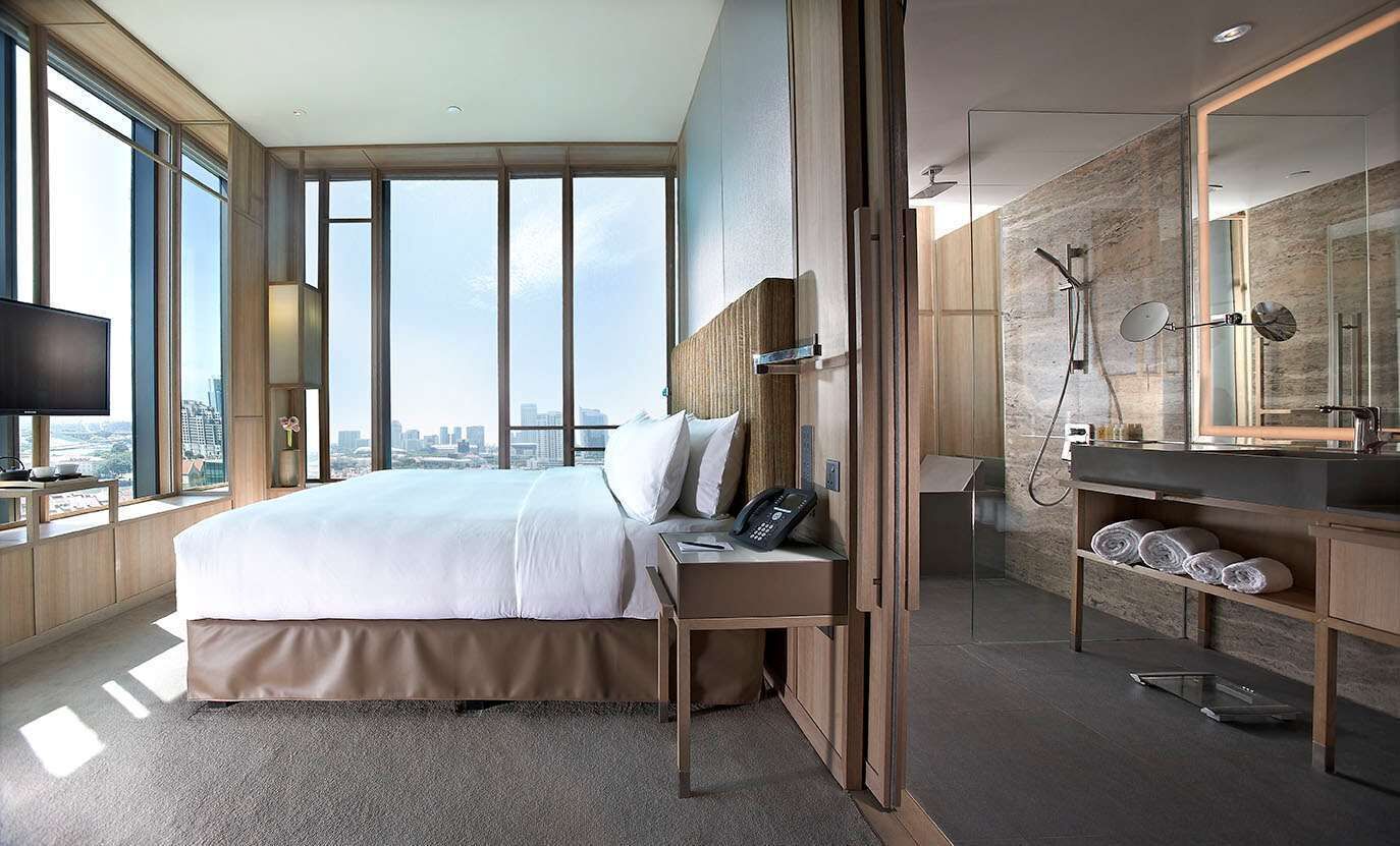 A modern hotel room with a large bed, a bathroom with a glass shower enclosure, and a city view.