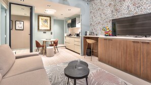 Una sala de estar moderna con un sofá, una mesa de centro y un comedor con sillas y una mesa. Se observa una cocina con armarios de madera y un televisor de pantalla plana grande.