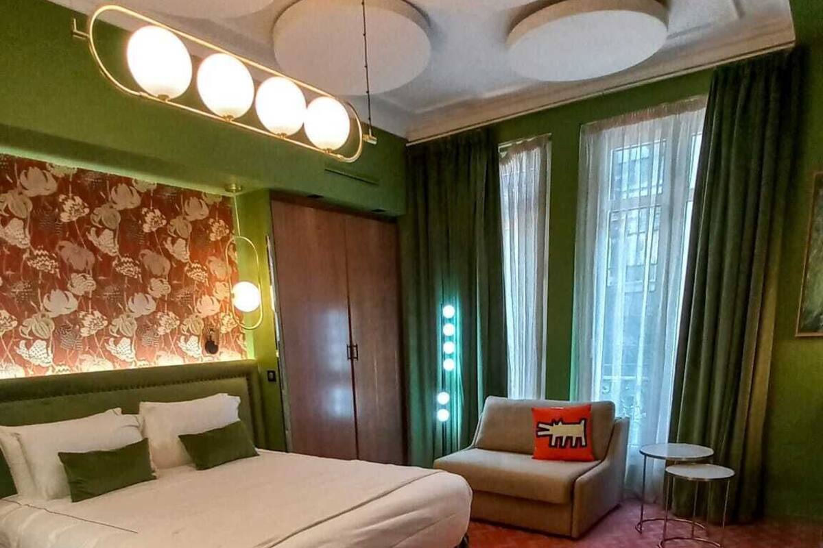 A hotel room with a large bed, a small sofa, a round table, and a mirror above the bed.